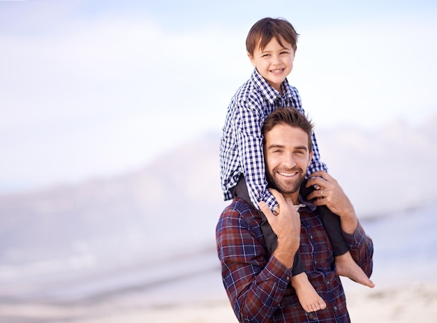 Portrait de plage et homme avec un enfant sur les épaules sourire et espace de maquette sur l'aventure en plein air Soutenir le visage du père et du fils dans la nature pour un lien amusant et une confiance heureuse pendant les vacances en mer ensemble