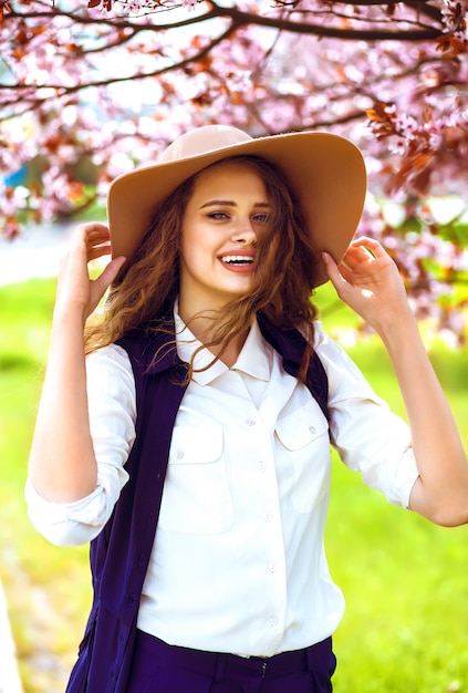 Portrait en plein air de la belle jeune femme à la mode posant près de l'arbre en fleurs.