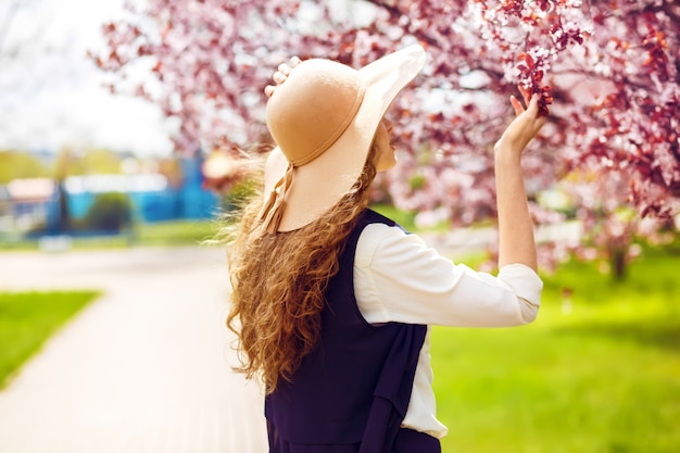 Portrait en plein air de la belle jeune femme à la mode posant près de l'arbre en fleurs.