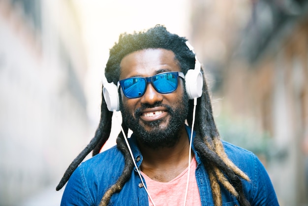 Portrait en plein air du beau jeune homme africain écoutant de la musique.