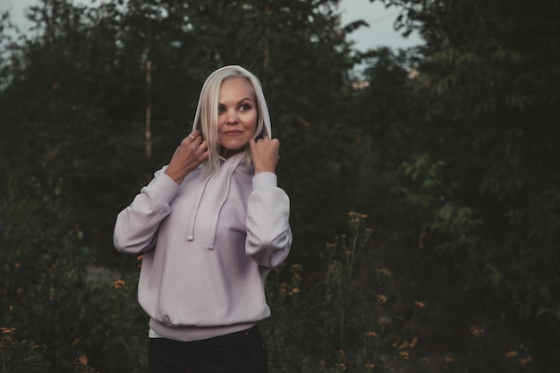 Portrait en plein air femme adulte sur la nature marchant dans la forêt d'été du crépuscule. Dame rêveuse en soirée à pied dans un parc. Émotion positive de la femme sur le parc à l'aube