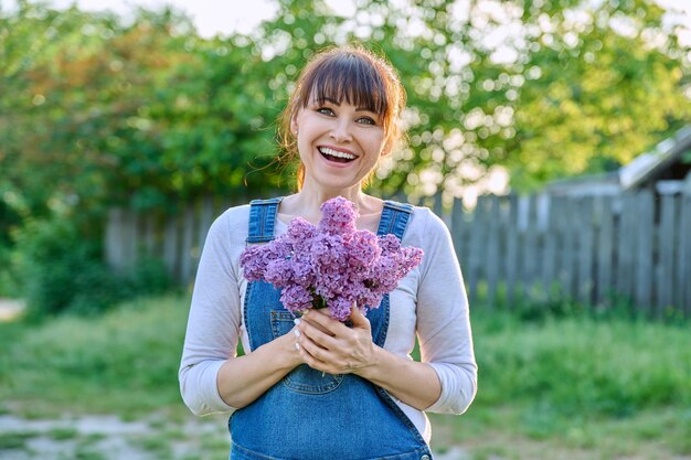 Photo portrait en plein air d'une femme mature heureuse avec un bouquet de lilas