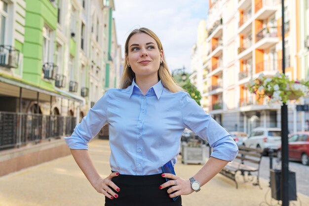 Portrait en plein air d'une jeune femme d'affaires confiante avec les mains jointes, fond de rue de la ville. Employé de bureau féminin en chemise bleue à l'écart