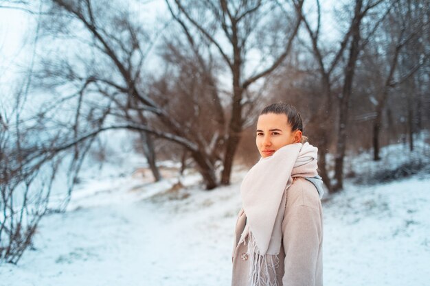 Portrait en plein air de jeune fille dans le parc en journée d'hiver, portant un foulard et un manteau, sur fond d'arbres.