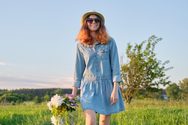 Portrait en plein air d'une jeune fille avec des fleurs marchant dans un pré ensoleillé