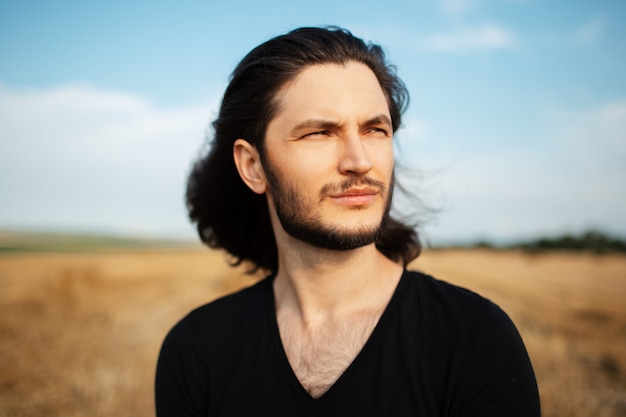 Portrait en plein air de jeune homme aux longs cheveux noirs, sur le terrain.