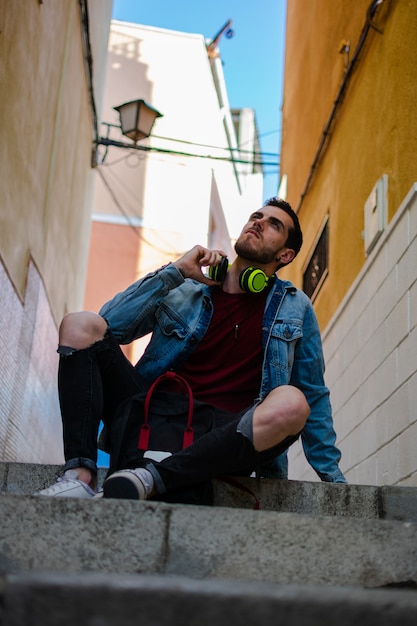 Portrait en plein air de jeune homme moderne avec un téléphone intelligent, assis dans la rue