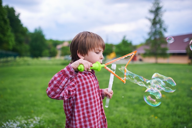Portrait en plein air de mignon garçon d'âge préscolaire soufflant des bulles de savon sur une pelouse verte