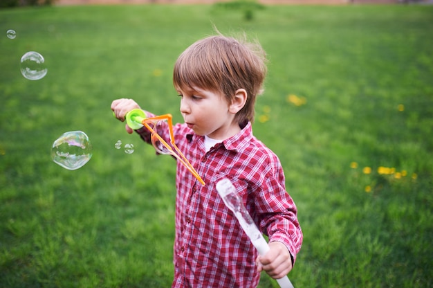 Portrait en plein air de mignon garçon d'âge préscolaire soufflant des bulles de savon sur une pelouse verte