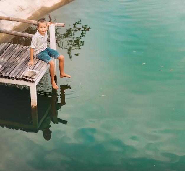 Portrait en plein air d'un petit garçon mignon assis sur une jetée d'un lac