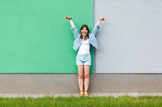 Portrait de pleine longueur d'une belle femme excitée dans un style denim jeans décontracté en été debout et pointant vers l'espace de copie de mur vert et bleu clair. deux concepts de choix différents.