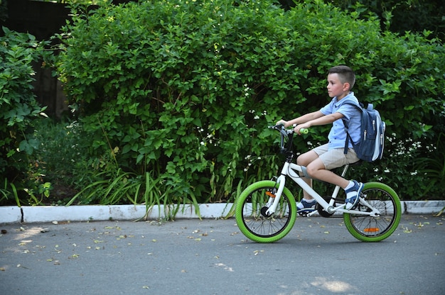 Portrait de pleine longueur de côté d'un écolier sur un vélo sur une route goudronnée tôt le matin. Garçon à vélo dans la ville