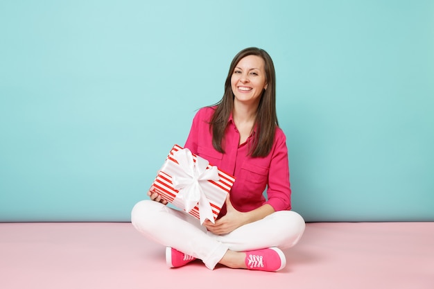 Portrait de pleine longueur femme en chemise rose chemisier pantalon blanc assis sur le sol tenir la boîte présente