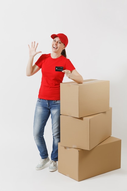 Portrait de pleine longueur de femme de livraison en casquette rouge, t-shirt isolé sur fond blanc. Courrier féminin près de boîtes en carton vides avec carte de crédit. Réception du colis. Copiez l'espace pour la publicité.