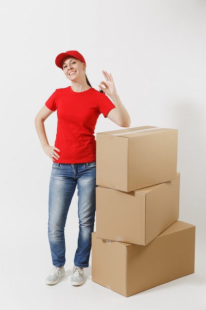 Portrait de pleine longueur de femme de livraison en casquette rouge, t-shirt isolé sur fond blanc. Coursier ou marchand féminin debout près de boîtes en carton vides. Réception du colis. Copiez l'espace pour la publicité.