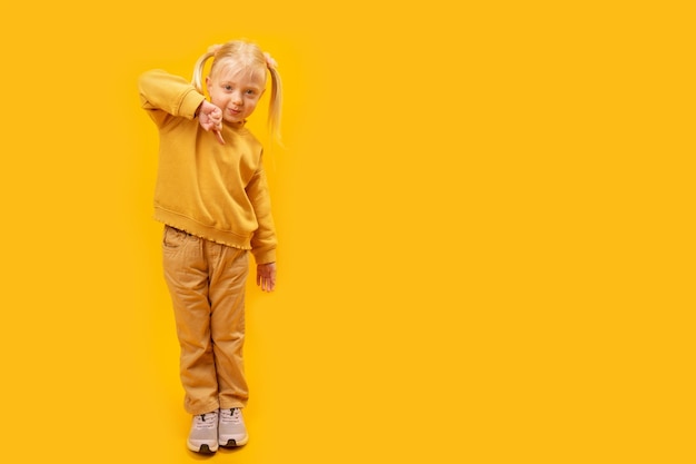 Portrait de pleine longueur de fille montre le doigt vers le bas Enfant de 45 ans en costume jaune sur fond jaune vif Copie espace maquette