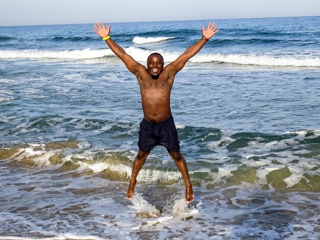 Photo portrait en pleine longueur d'un homme sans chemise sautant sur la plage