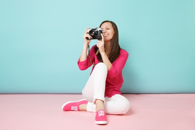 Portrait de pleine longueur jeune femme en chemise rose chemisier pantalon blanc assis sur le sol tenir l'appareil photo