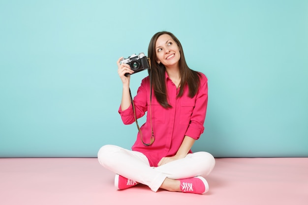 Portrait de pleine longueur jeune femme en chemise rose chemisier pantalon blanc assis sur le sol tenir l'appareil photo