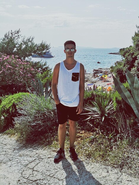 Photo portrait en pleine longueur d'un jeune homme debout près des plantes contre la mer