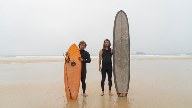 Photo portrait en pleine longueur de surfeurs debout avec des planches de surf à la plage