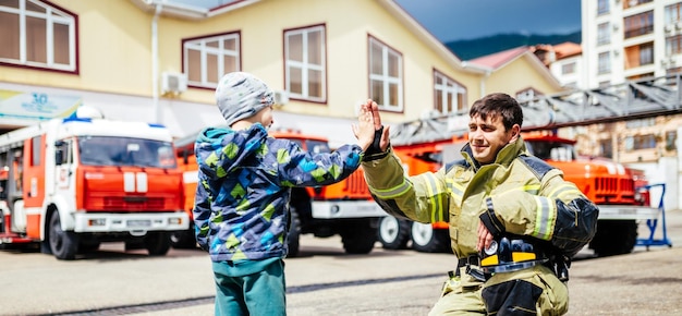 Portrait d'un pompier avec un enfant debout sur fond de camions de pompiers dont Childs rêvait