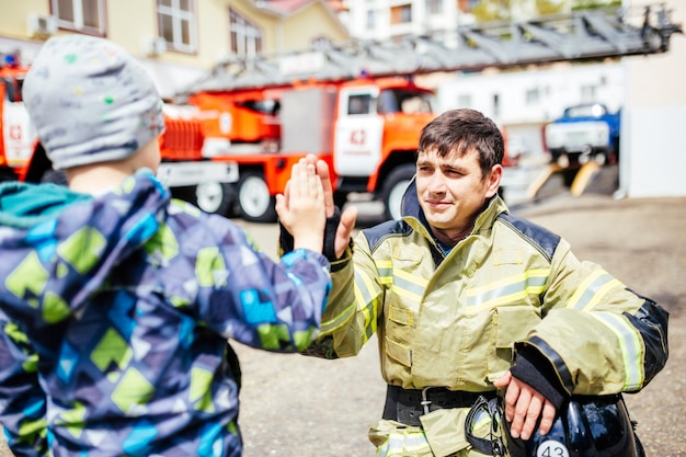 Portrait d'un pompier avec un enfant debout sur fond de camions de pompiers Rêves d'enfants