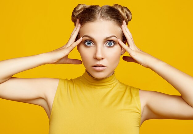 Portrait positif du magnifique modèle de femme blonde hipster aux cheveux bouclés posant sur fond jaune coloré en studio