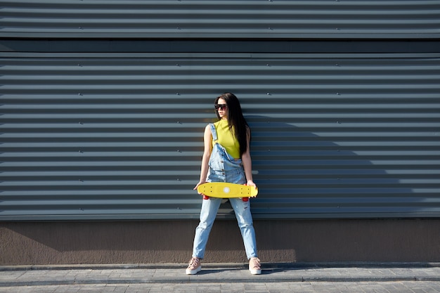 Portrait de positive jeune jolie fille vêtue d'un jean jaune haut et bleu avec une planche à roulettes jaune.