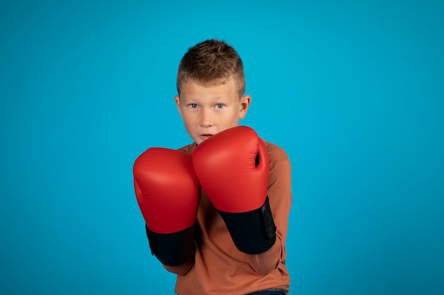 Portrait d'un préadolescent motivé portant des gants de boxe posant sur fond bleu