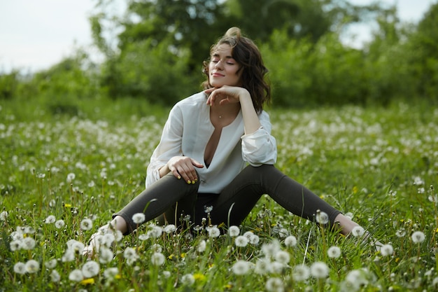 Portrait De Printemps D'une Femme Assise Dans Un Champ Sur L'herbe Parmi Les Fleurs De Pissenlit. Femme Joyeuse Aime Le Temps De Printemps Ensoleillé. Beauté Naturelle D'une Femme, Cosmétiques Naturels