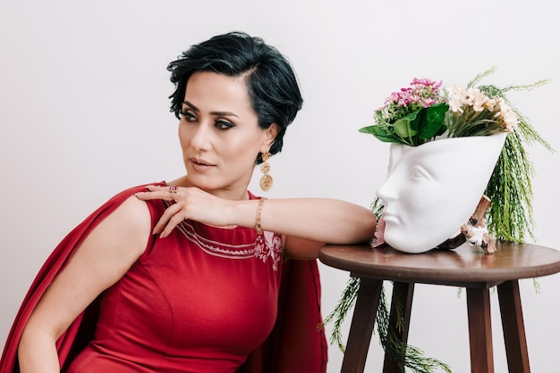 Portrait de printemps d'une jeune femme en robe rouge élégante posant avec un vase en plâtre avec des fleurs