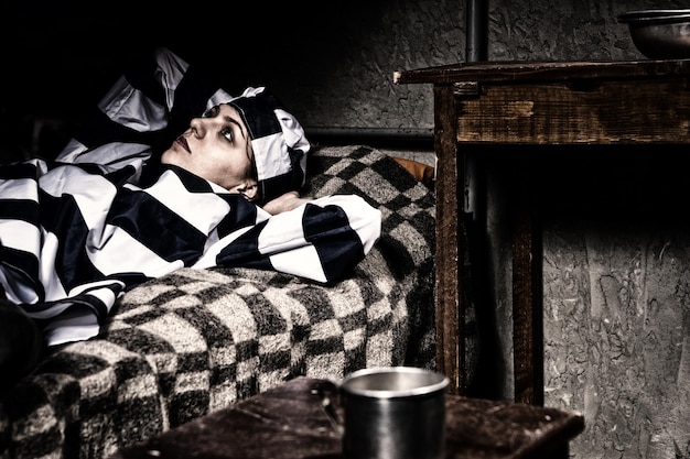 Portrait d'une prisonnière portant un uniforme de prison a perdu ses pensées alors qu'elle était allongée dans son lit près d'une table de chevet avec des plats en aluminium dans une cellule de prison