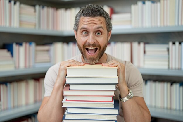 Photo portrait d'un professeur drôle avec un livre dans la salle de classe de la bibliothèque un professeur beau dans la bibliothèque de l'université un enseignant drôle tenant beaucoup de livres un enseignant fou avec des livres des enseignants excités dans la bibliothéque de lécole