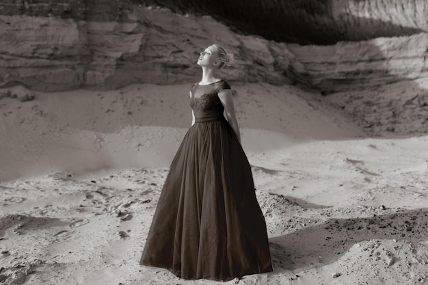 Portrait de profil d'une belle jeune femme, en robe longue rouge, posant dans un désert de sable.