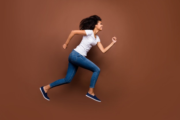 Portrait de profil complet du corps d'une femme à la peau foncée drôle folle sautant des compétitions sportives de haut niveau participant se précipiter pour finir porter un jean t-shirt blanc