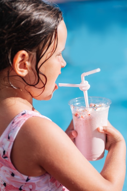 Portrait de profil d'une fille de race blanche buvant un cocktail avec une paille sur la plage au bord de la mer sur un t...