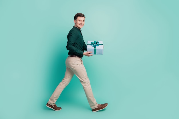 Portrait de profil d'un gars joyeux étape tenir la caméra de regard de boîte-cadeau sur fond turquoise