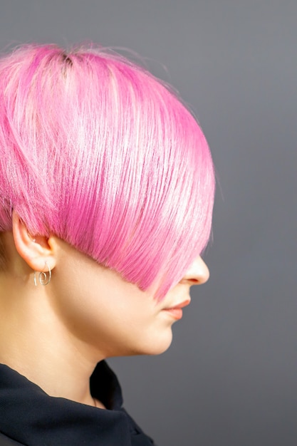 Portrait de profil d'une jeune femme de race blanche avec une coupe de cheveux rose isolée sur fond gris.