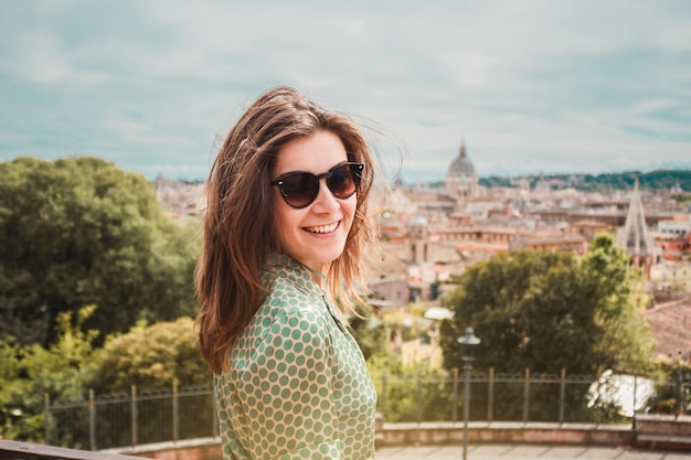 Photo portrait de profil d'une jeune femme souriante en lunettes de soleil avec une vue panoramique sur rome, en italie