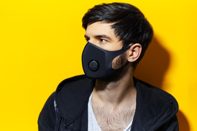 Portrait de profil en studio de jeune homme portant un masque respiratoire de couleur noire, contre le coronavirus. Fond de couleur jaune.