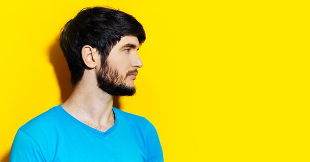 Portrait de profil en studio de jeune homme à la recherche d'aqua à fond vide de couleur jaune avec espace de copie.