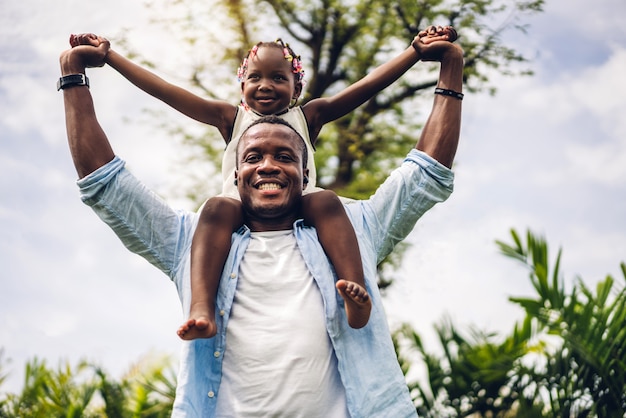 Portrait de profiter de l'amour heureux famille noire père afro-américain portant fille petite fille africaine enfant souriant et s'amusant des moments de bon temps dans le parc d'été à la maison