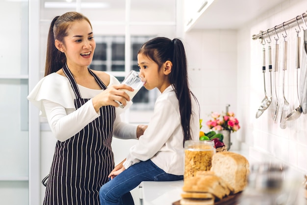 Portrait de profiter de l'amour heureux mère de famille asiatique et petite fille asiatique fille enfant souriant et prendre le petit déjeuner boire et tenir des verres de lait à table dans la cuisine