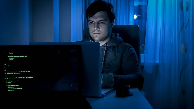 Portrait d'un programmeur masculin ou d'un pirate informatique travaillant la nuit sur un ordinateur