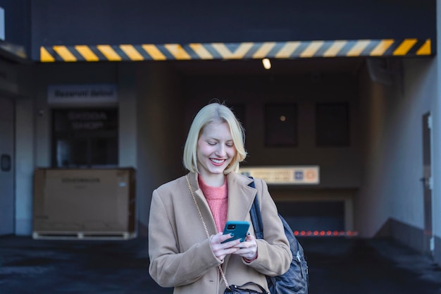 Portrait recadré d'une belle journaliste au travail Regardant son smartphone Jeune femme debout dans la rue et souriant Prise de vue horizontale Mise au point sélective sur la femme