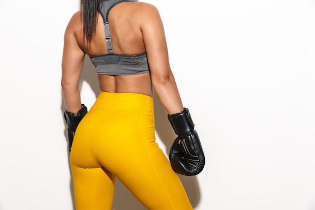 Portrait recadré d'un boxeur de femme de fitness sportif jeune et fort isolé sur un mur blanc dans des gants.