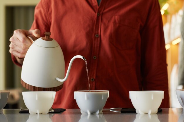 Portrait recadré d'une femme barista versant du café dans des tasses en rangée sur un support de bar, espace pour copie