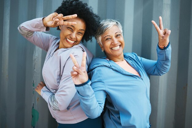 Portrait de remise en forme et amis seniors avec signe de paix se liant et posant après l'entraînement ou l'exercice ensemble Bonne forme physique et athlètes féminines âgées avec un geste de la main hipster après l'entraînement par le mur