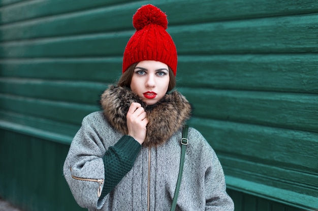 Portrait rétro d'une belle fille dans un chapeau rouge et un manteau debout près d'un mur en bois vert